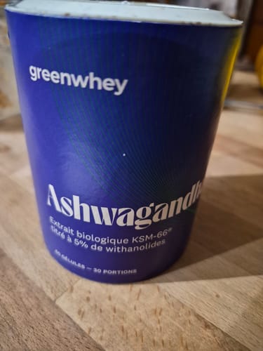 Customer's blue cylindrical container of greenwhey Ashwagandha bio KSM-66, sitting on a wooden surface.