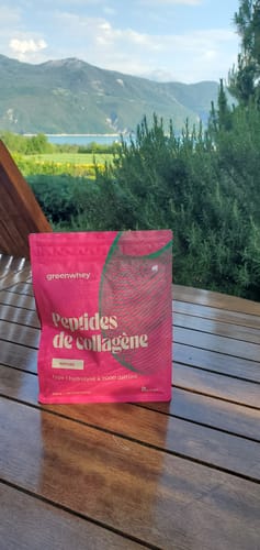 Avis d'un client sur le sachet rose de Peptides de Collagène, posé sur une table en bois en extérieur avec des montagnes en fond.