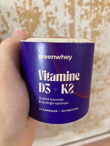 Client tenant dans sa main le pot violet de Vitamine D3 + K2 de greenwhey.