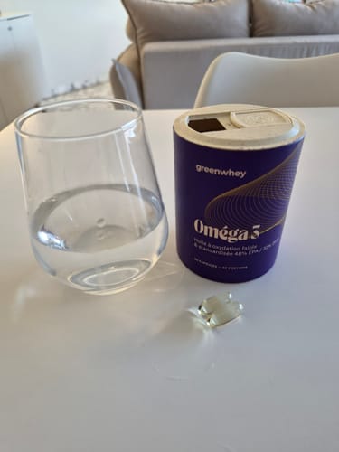 Le pot d'Oméga 3 EPAX® d'un client avec une gélule et un verre d'eau sur une table.