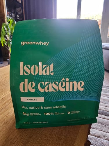 Photo d'un client montrant le sachet vert de l'Isolat de Caséine saveur vanille sur une table en bois.