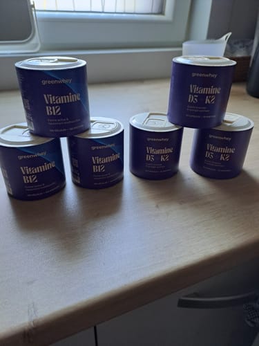 Client montrant plusieurs pots de Vitamine D3 + K2 sur un comptoir de cuisine.