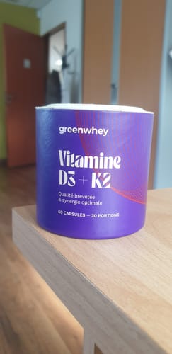Pot en carton violet de vitamine D3 et K2 Greenwhey posé sur une table en bois.