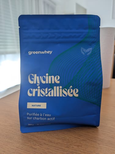 Photo d'un client montrant le sachet bleu de Glycine cristallisée, posé sur une table en bois.